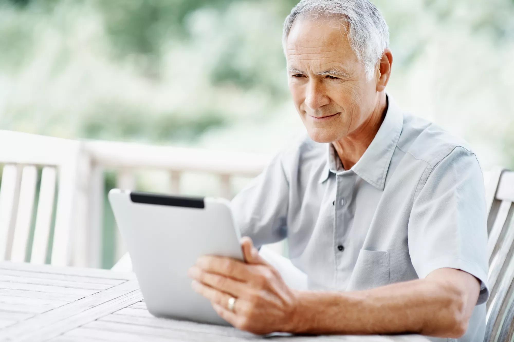 Old man sitting outside and looking at a tablet.