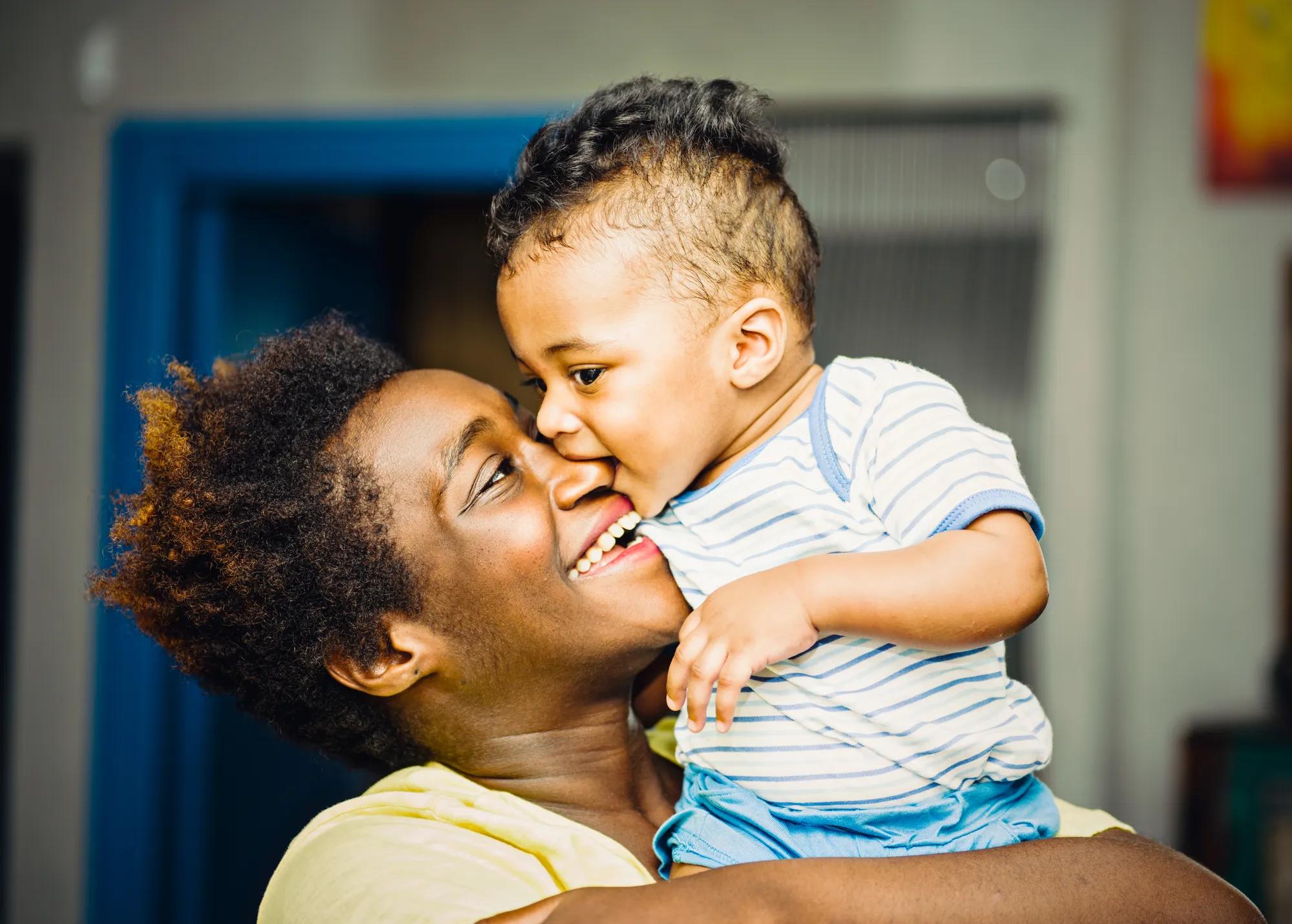 Black mother holding her infant son in her arms and snuggling with him