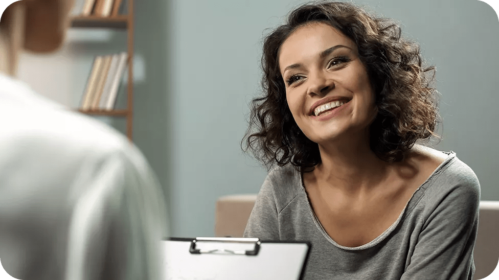 Patiente souriante avec cheveux bruns bouclés tombant aux épaules en discussion avec son médecin