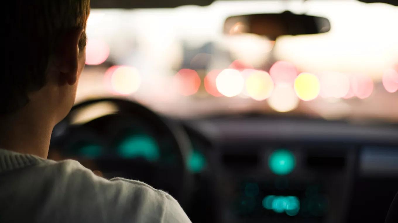 An over-the-shoulder view of a man driving his car around sunrise