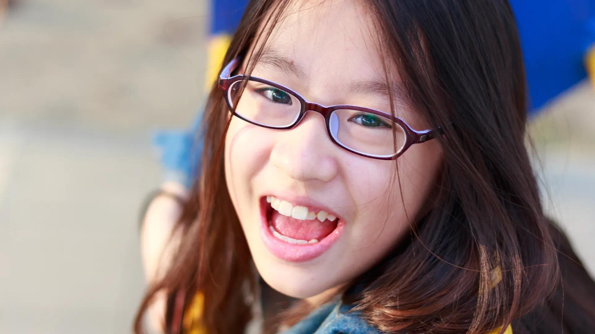 A close-up of an Asian girl on a playground wearing glasses