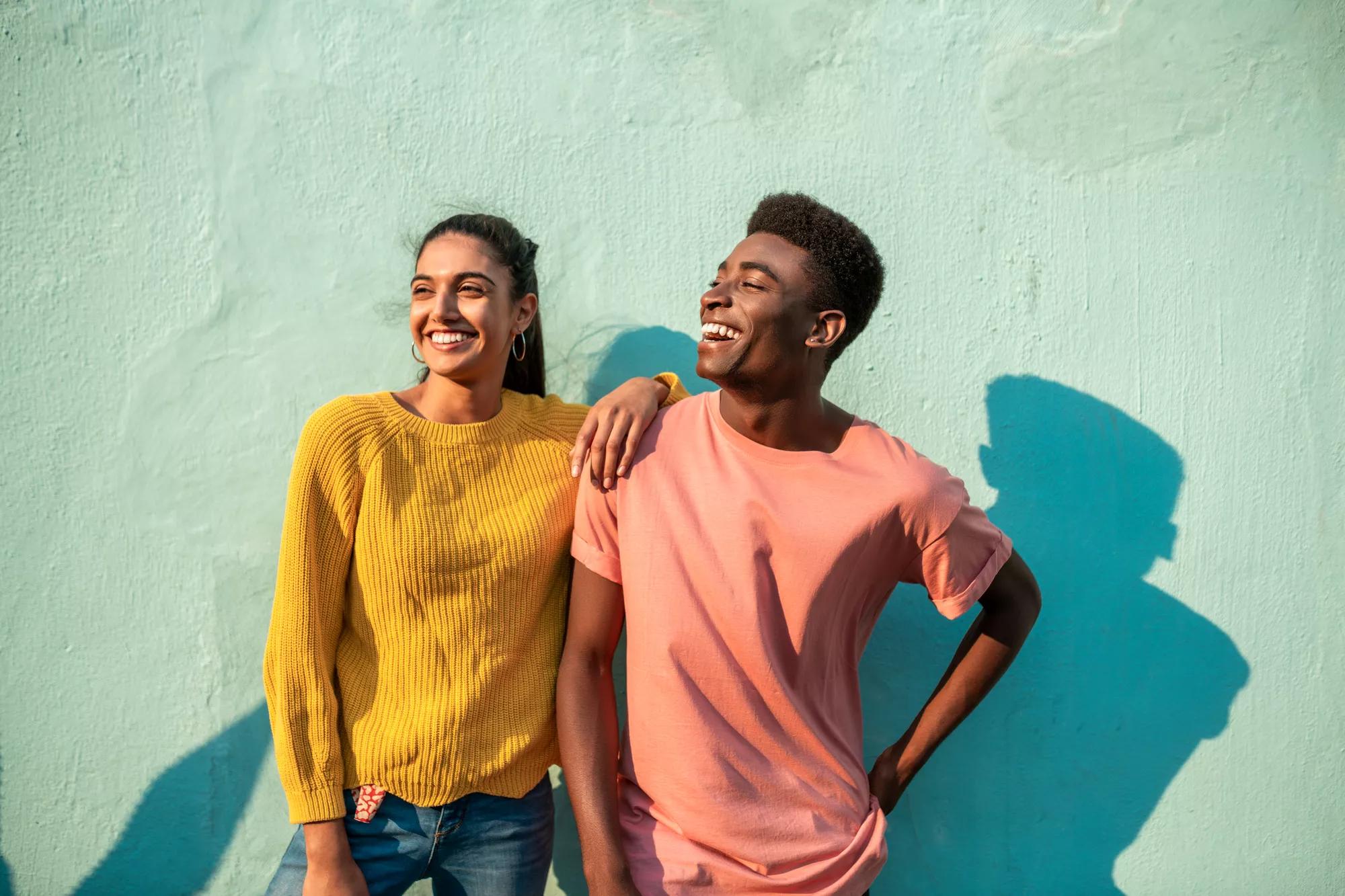 Moça e rapaz sorrindo contra uma parede verde 