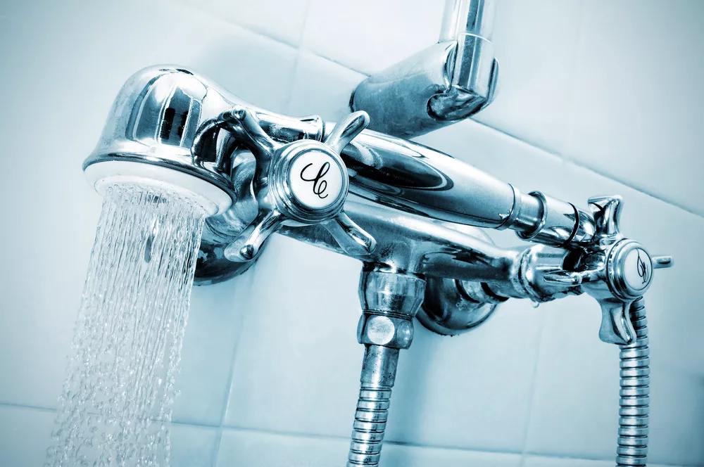 A close-up of a silver shower head with water coming out laid across the hot and cold handles