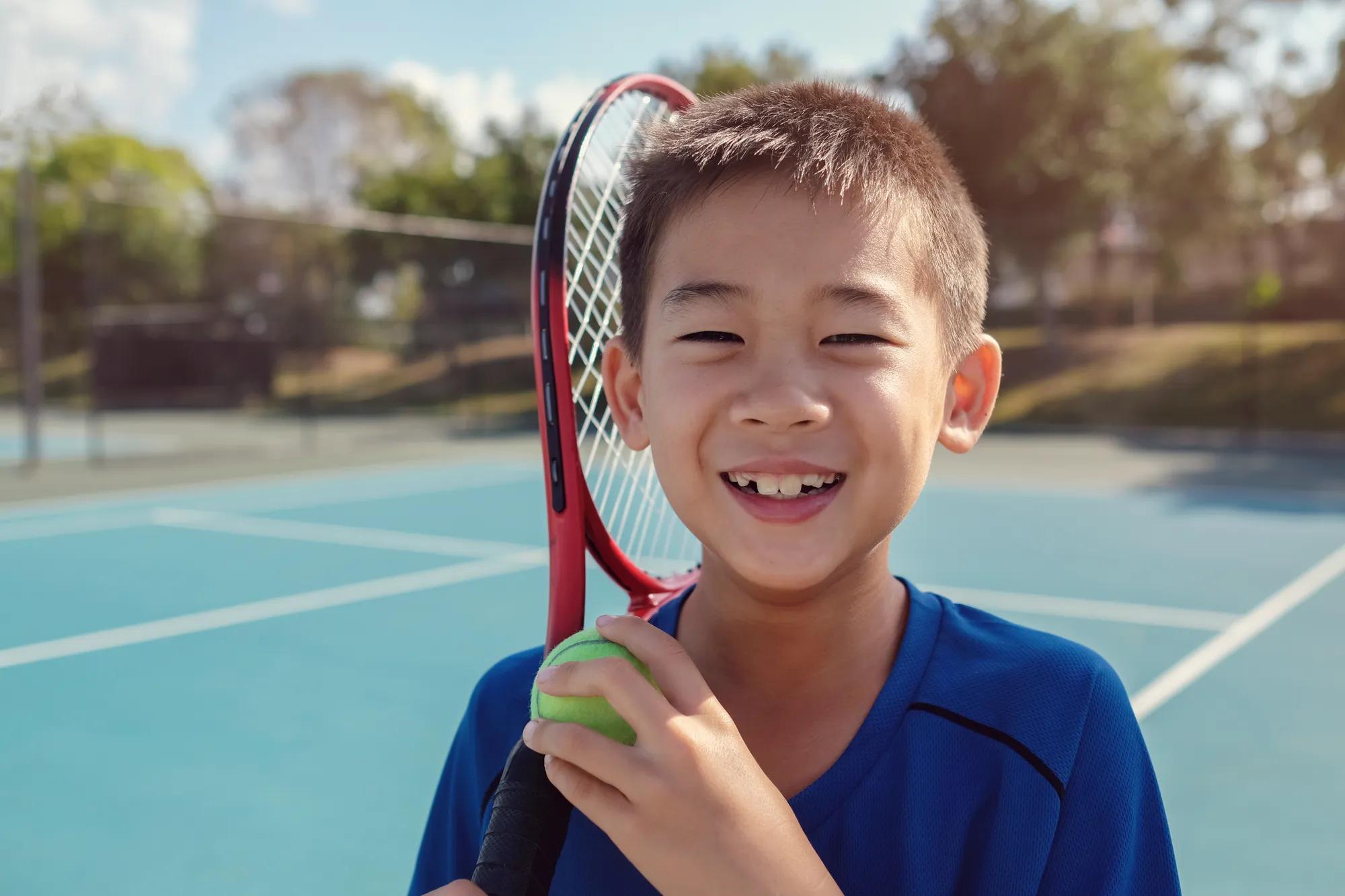 Young tween Asian boy tennis player on outdoor blue court