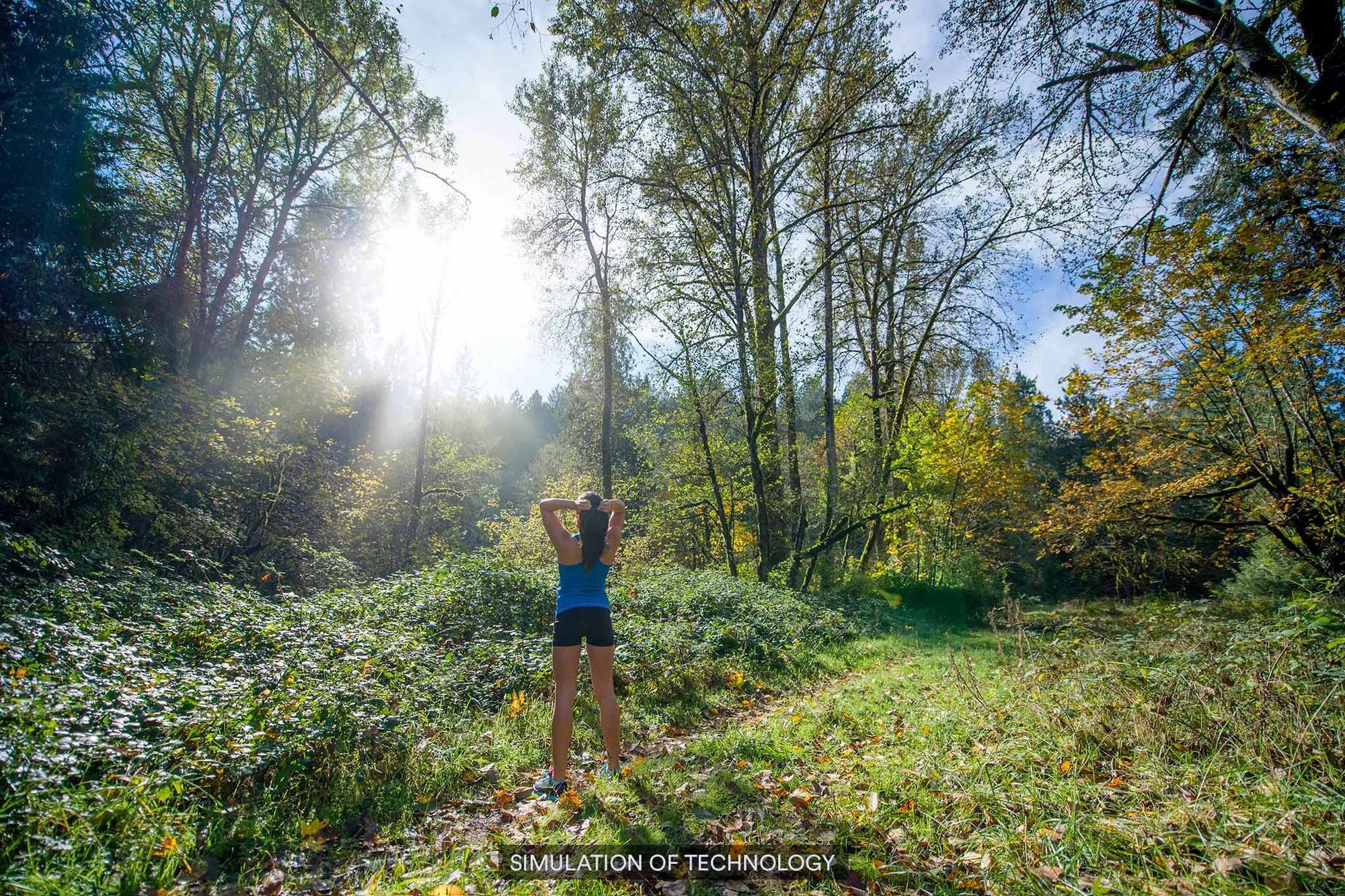 A woman hiking in the forest with sunlight beaming through the trees, but blurry.