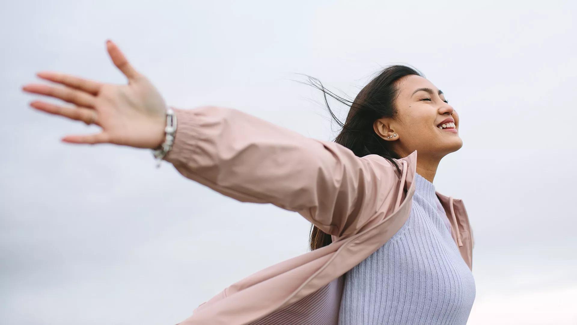 A young Asian woman with grey shirt smiling and enjoying the breeze at the open space