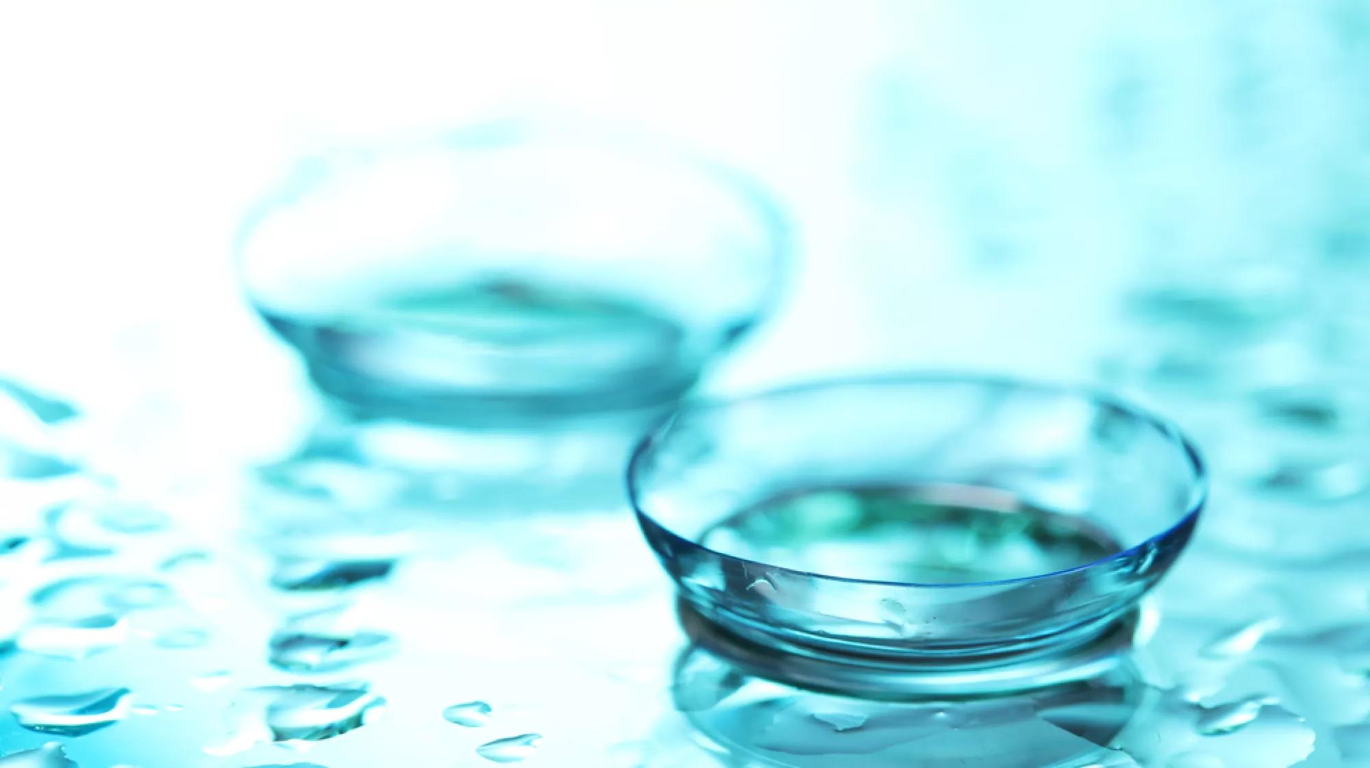 A close-up of two contact lenses on a wet, blue surface 