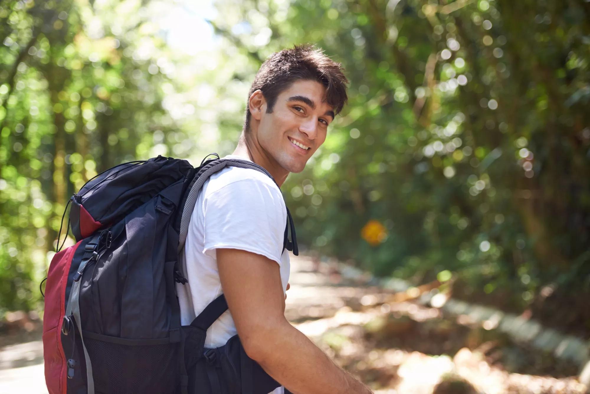 Smiling young man with a black backpack on his back. Smiling young man with a white shirt, carrying a black backpack on his back.