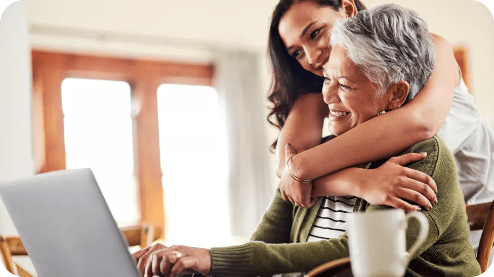 Mãe e filha se abraçando e rindo enquanto olham para a tela de um computador