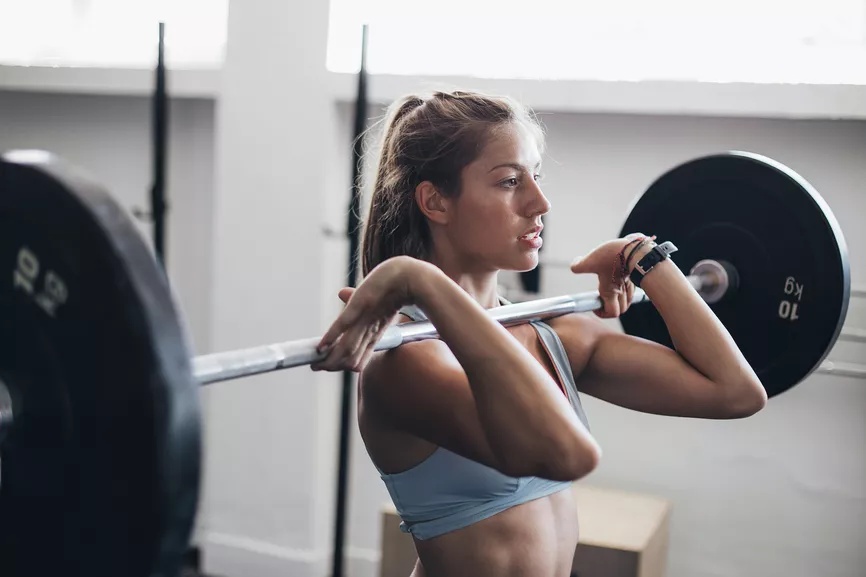 A young woman lifting a barbell in a gym