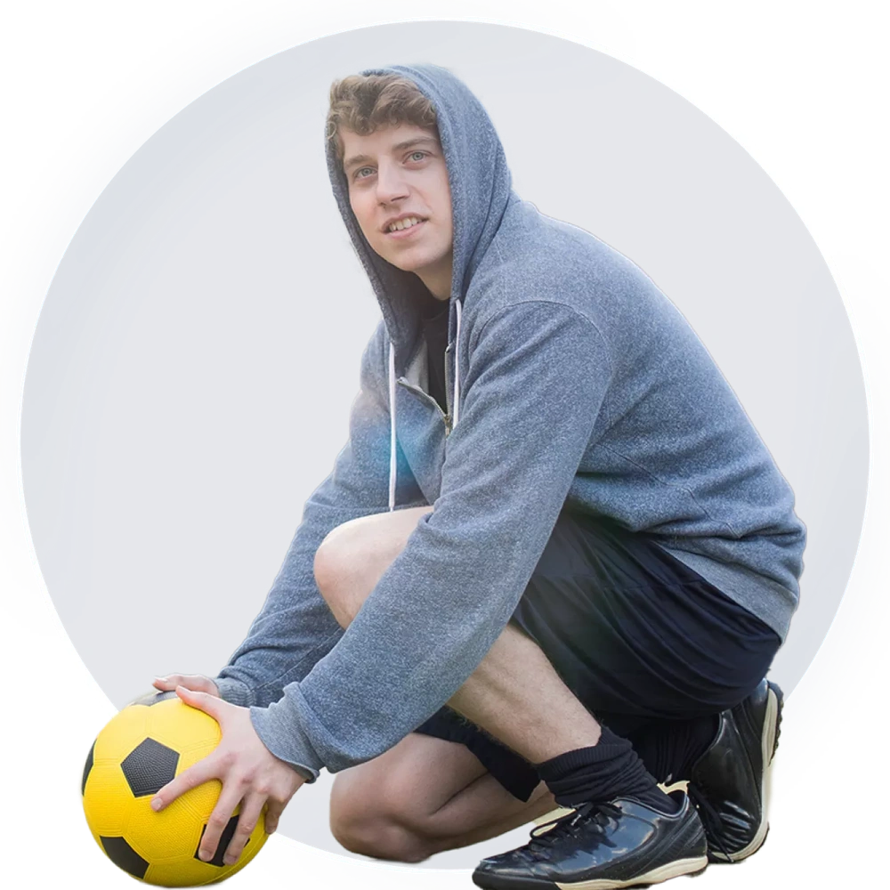 Boy wearing a hoodie and shorts picking up a ball in a playground