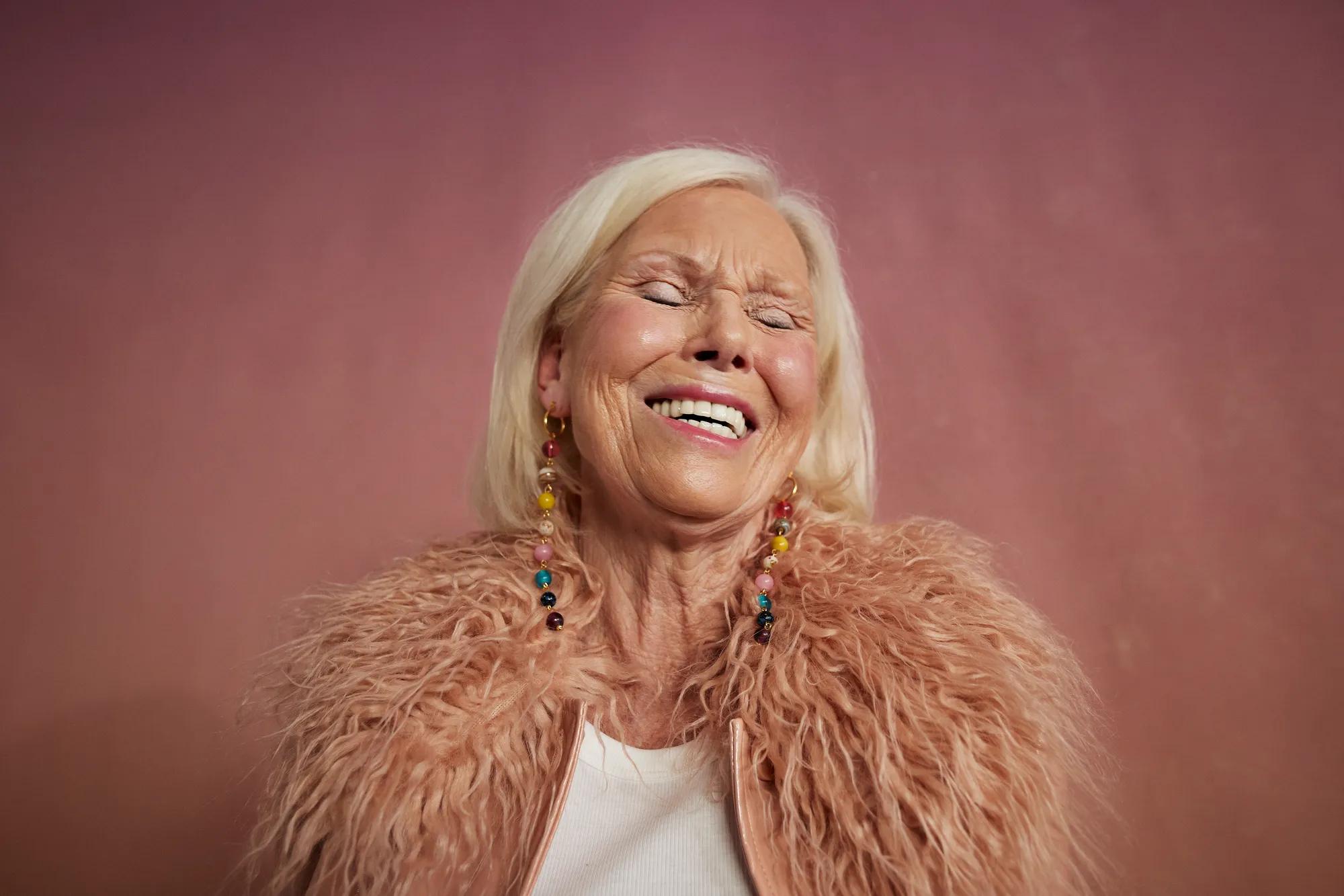 An older woman laughs with pink fur on her shoulders