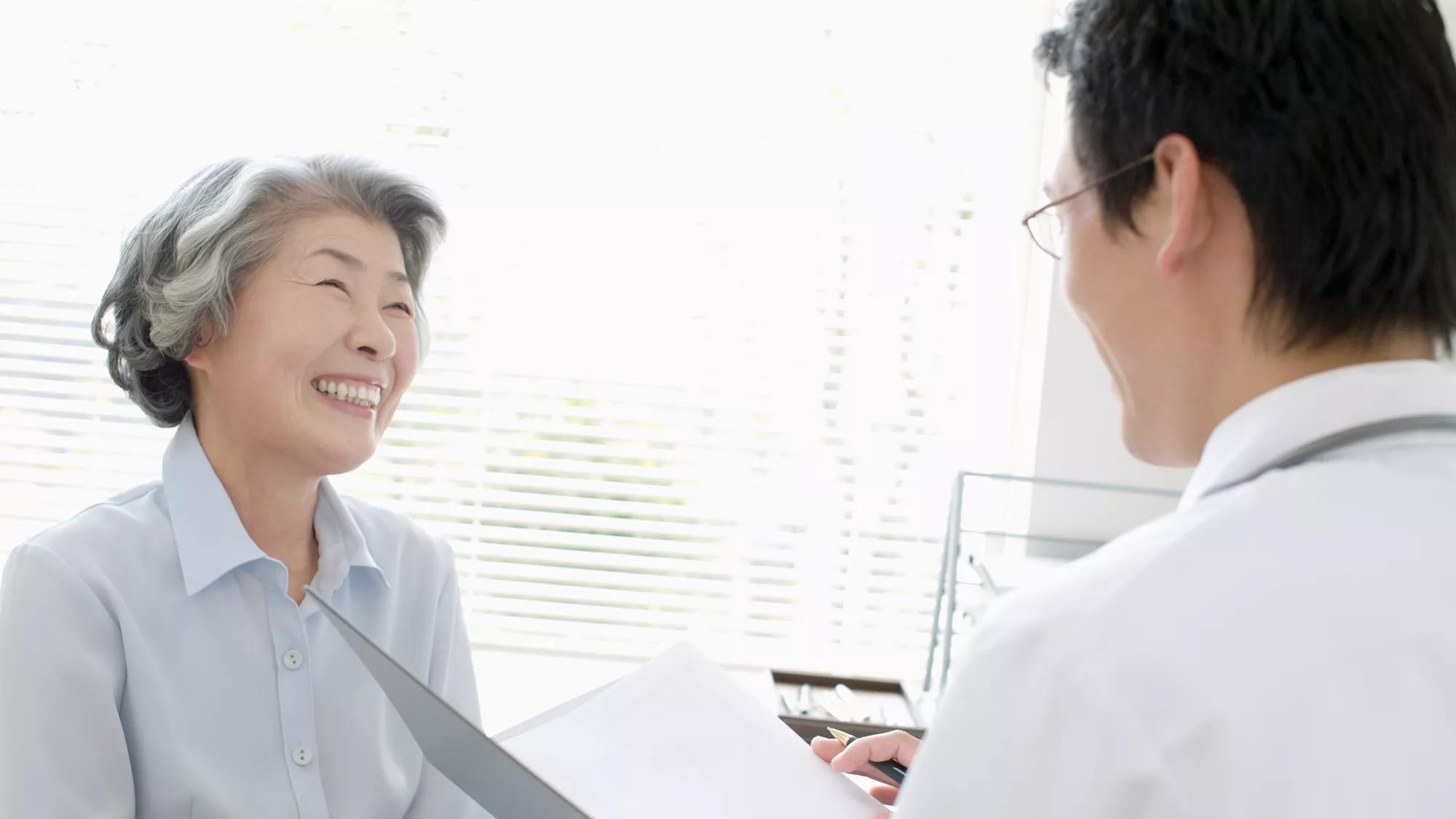 An older Asian woman with grey hair smiles at a young male eye doctor