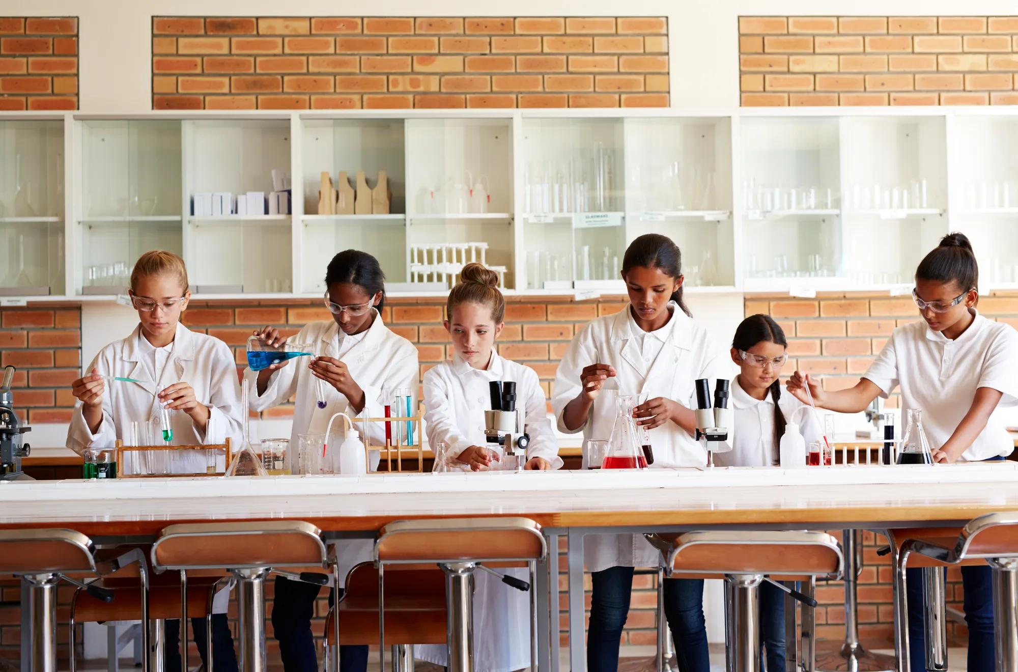 A row of children in labcoats do science experiments in a school science class