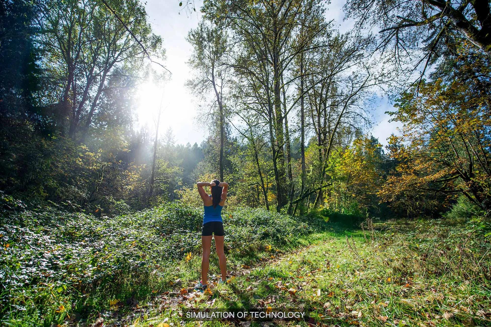 A woman hiking in the forest with sunlight beaming through the trees.