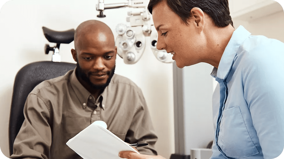 A female eye doctor sits with a Black man in the exam room looking over paperwork together